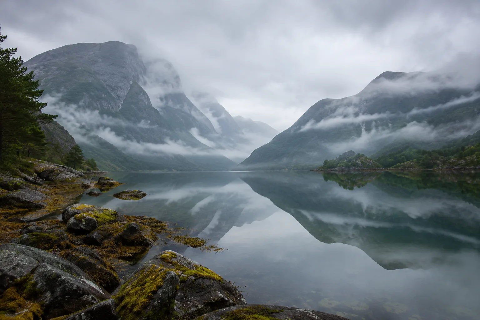 Fjord embrumé aux eaux immobiles, montagnes fondues dans le gris-vert