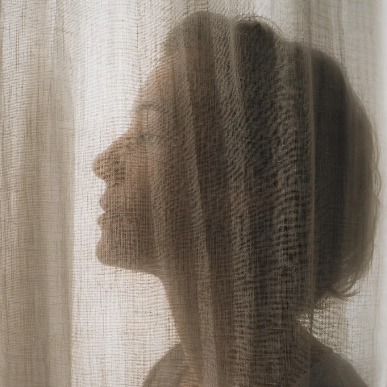 Visage de profil derrière un voilage, contours adoucis par le tissu